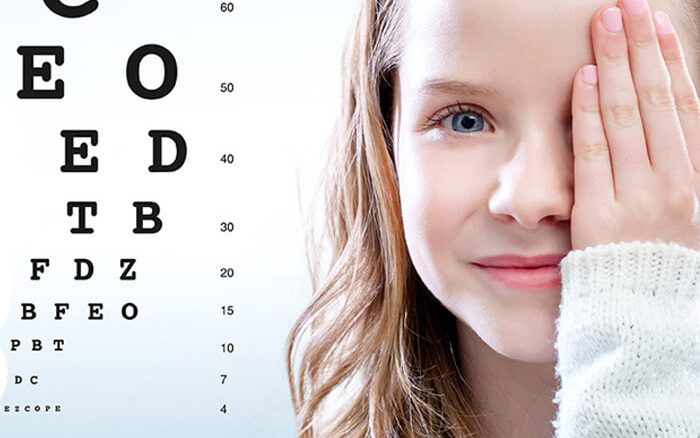 Young girl covering one eye with eye chart