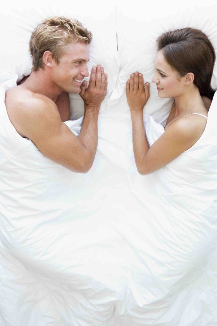 A man and woman laying in bed with their hands touching.