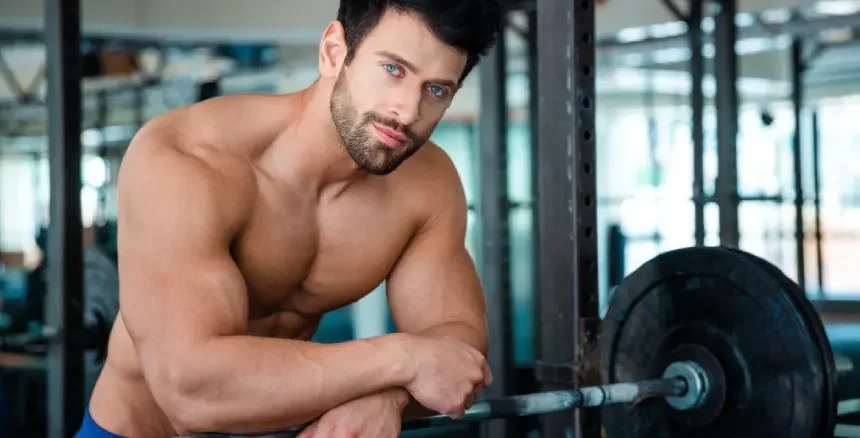 Muscular man posing with barbell in gym.